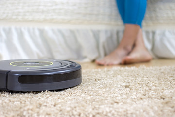 The automatic robot vacuum cleaner cleans the carpet while the housewife is resting on the couch