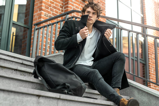 Pensive Man Sitting On Concrete Steps And Wrapping Up In Black Coat