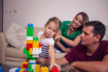 Playing family- mother and father playing with cute daughter cubes together at home.