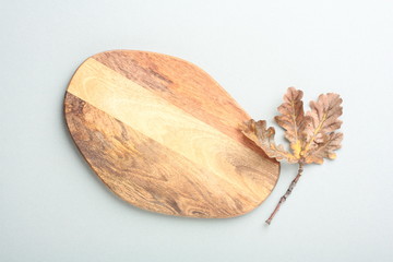 Wooden cutting board with a branch of autumn leaves on a gray background
