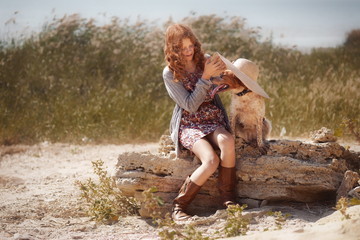 Red-haired beautiful girl in a hat in the autumn on nature with a red hunting dog sitting on a rock