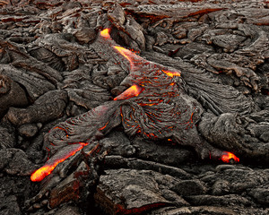 A lava flow emerges from an earth crevice and flows in a black volcanic landscape, glowing magma,...