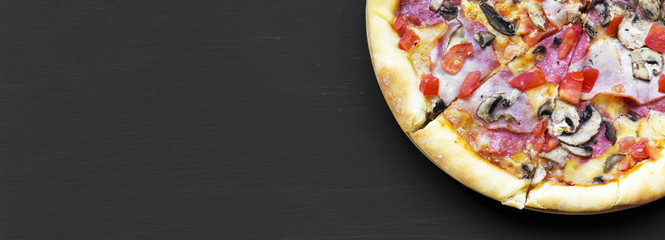 Freshly baked pizza on black background, close-up. Flat lay, overhead, from above. Copy space.