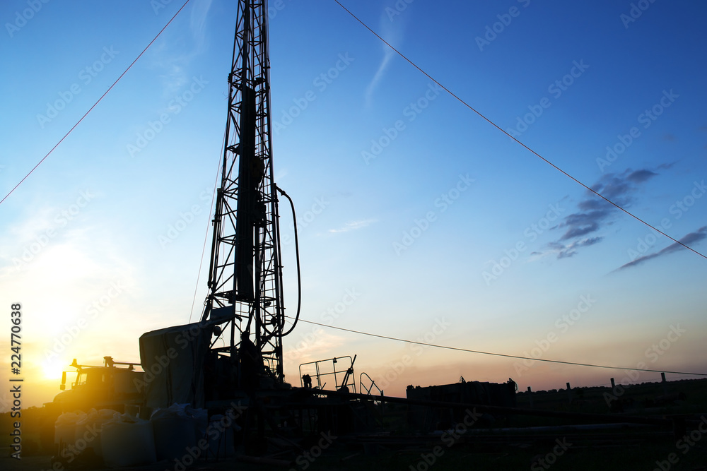 Wall mural drilling rig drills a well to extract water at sunset in the rays of the setting sun. Water supply of the population