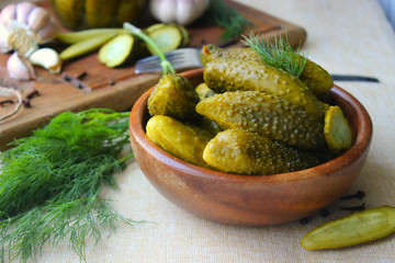 Cucumbers in a wooden bowl, fresh herbs, pickling spices and jars of pickled cucumbers on the table