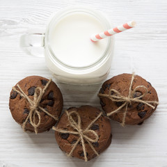Chocolate chip cookies and glass jar of milk on a white wooden table, overhead view. Closeup.