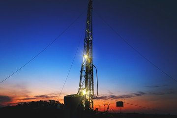 drilling rig drills a well for the extraction of drinking water at sunset under a beautiful sky for...