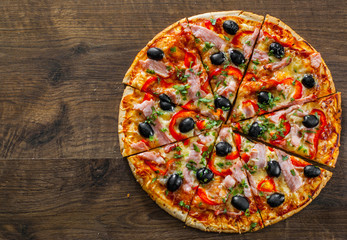 slices of Pizza with Mozzarella cheese, ham, pepper, meat, Tomatoes, olives, Spices and Fresh Basil. Italian pizza on wooden background