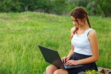 beautiful young woman sitting on grass with laptop