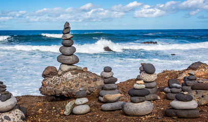Delicately balanced man made stacks or piles of stones with crashing waves in the background