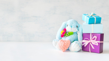 Cute toy soft blue bunny with a flower and pink thread heart with soap bubbles on light background....