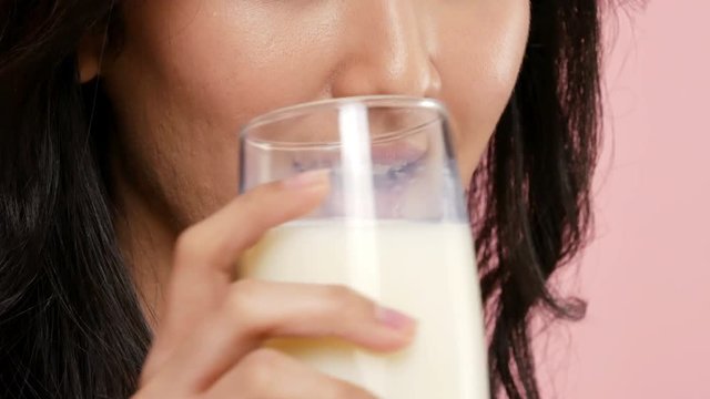 Asian woman enjoying fresh glass of milk at pink background. People with healthcare and beauty concept.