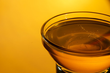 Glass bowl with honey on a bright yellow background close-up with copy space