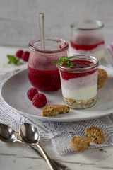 Vassoio bianco con vasetti di vetro con yogurt, cereali e salsa di lamponi