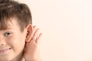 Fototapeta premium Cute little boy with hearing problem on light background, closeup. Space for text