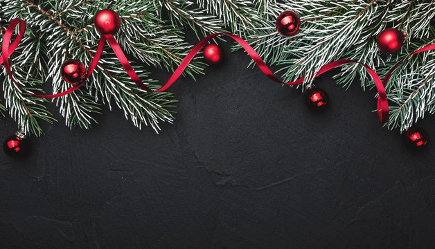 Horizontal black stone background with fir branches decorated with red balls. Top view. Space for text