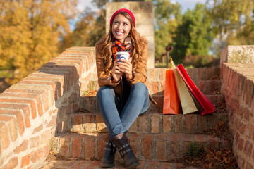 Beautiful young woman sitting on stairs outside while drinking a coffee after shopping