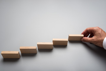 Businessman placing wooden pegs or dominos on grey surface