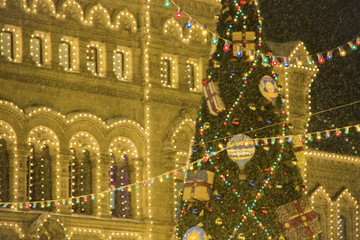 Christmas decorations on a facade, big xmas tree with balloonы and presents blurry. New Year in Moscow, Russia. Heavy snowfall.