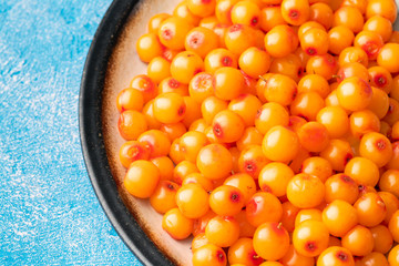 Sea-buckthorn berries in bowl and natural honey or sea buckthorn oil on blue background