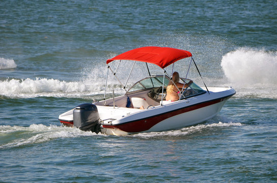 Sporty runabout motor boat with red canvas canopy powered by a single outboard engine.