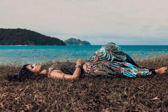 beautiful young boho woman lying on a grass at the beach