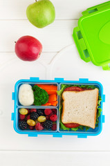 Open lunch box with sandwich, vegetables, egg, fresh berries on the white wooden background with copy space. Top view, flat lay.