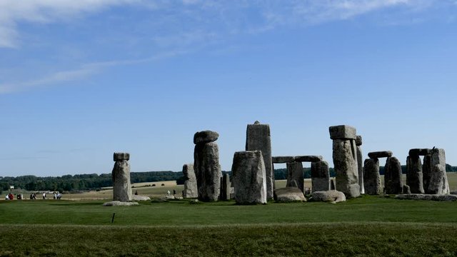 Time lapse-Shadows from passing clouds pass over the Stonehenge prehistoric monument as far-distant unidentifiable visitors seem to scurry around like frantic ants