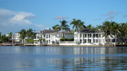 Fototapeta na wymiar Typical luxury riverfront summer homes along quiet river in tropical southern location on beautiful summer day. Exterior generic establishing shot