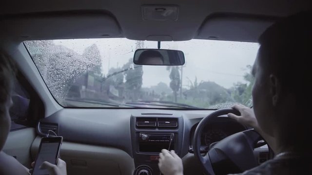 Young caucasian attractive woman and cute man dressed in colored t-shirts are sitting in new car and riding in rural road at eastern, tropical area on rainy summer day