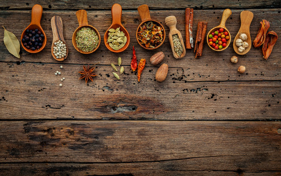 Various herbs and spices in wooden spoons on wooden background.