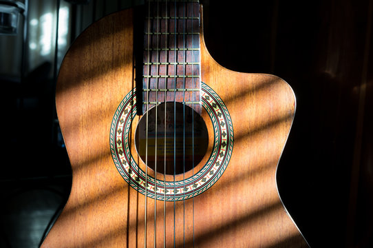 Close up of handmade classical guitar with striped shadows across the body and neck of the instrument