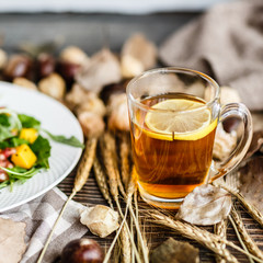 Salad with mango, arugula, pomegranate seeds lying on white plate. Next lying pumpkin, cup of black tea with lemon, dry flowers and leaves, physalis, chestnuts, sweater