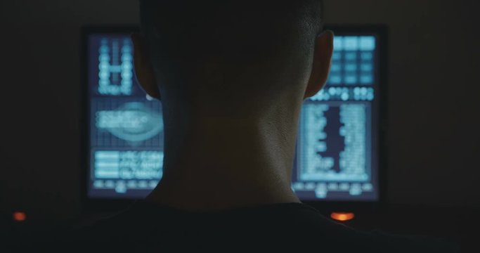 hacker works at a computers in a dark office room.