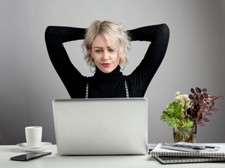 Young attractive woman with laptop sitting at a desk with a confused, unsure attitude.