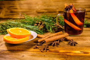 Cup of mulled wine with cinnamon, sliced orange and fir tree branches on wooden table