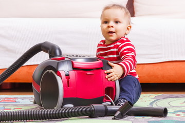 Happy little baby boy on carpet at home and vacuum cleaner with accessories