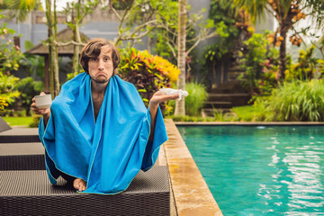 Sick man traveler. The man caught a cold on vacation, sits sad at the pool drinking tea and blows...
