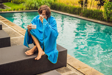 Sick man traveler. The man caught a cold on vacation, sits sad at the pool drinking tea and blows...