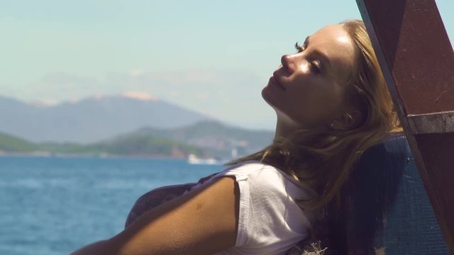 Beautiful woman relaxing on sailing ship on sea landscape. Young woman enjoying sailing on board of sea ship. Blue ocean and gren hills background.