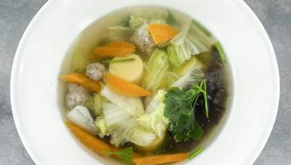 Clear Soup with Tofu and Minced Pork in a white plate on stone background. Thai foods. Close up Top view..