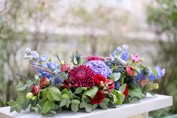 Elongated floral arrangement in vintage metal vase. table setting. Blue and red color. Gorgeous bouquet of different flowers. Park on background