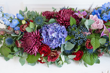 Elongated floral arrangement in vintage metal vase. table setting. Blue and red color. Gorgeous bouquet of different flowers. Bright room, stucco on the wall