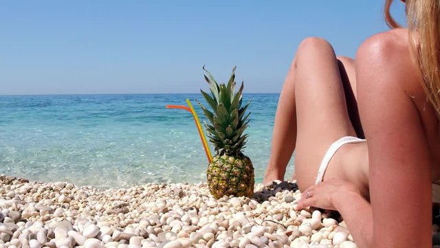 Sexy woman lying on a pebble beach with pineapple cocktail beside her