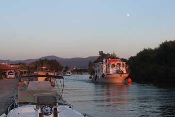 Fototapeta na wymiar Boat with tourists in the mythical river of Acheron is about to enter the Ionian sea at the village of Ammoudia in Preveza, Greece at sunset with full moon at the sky
