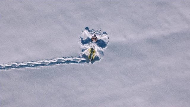 Aerial - Young woman falls on her back and starts making snow angel