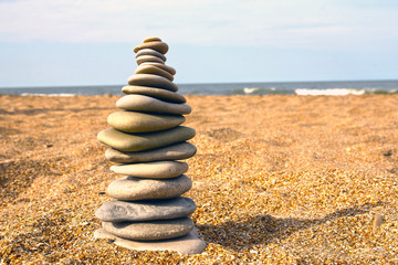 Fototapeta na wymiar Stones pyramid on sand symbolizing zen, harmony, balance. Sea in the background