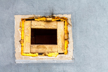 A square hole with wooden blocks in a brick wall painted with gray paint.