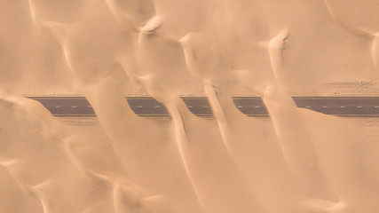 Aerial view of a desert road being run over by sand dunes photographed from a drone at sunrise....