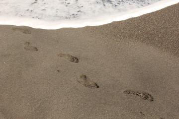the background image is white the sea foam of the waves lapping on the sandy beach, washing away the footprints in the sand